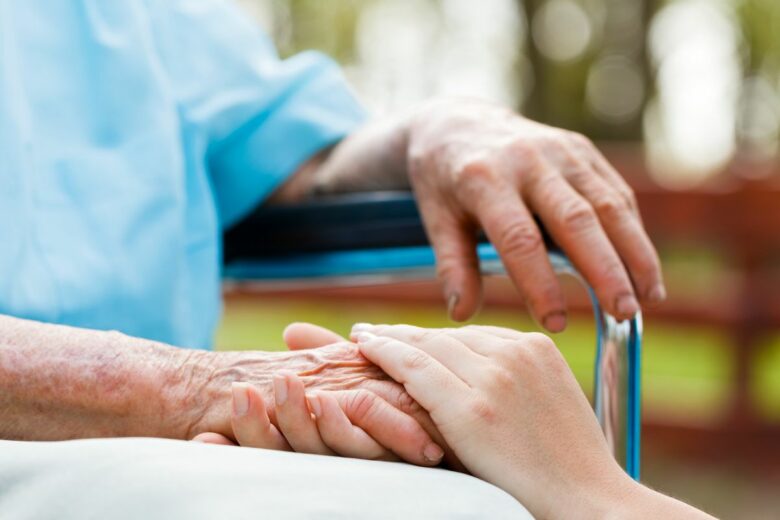 Hands of Nurse on Elderly Woman's Hands in Wheelchair Offering Homemaker Companionship Service in Florida