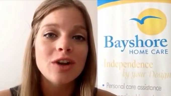 Breck, a senior care specialist, gives a tip while standing by a Bayshore Home Care banner