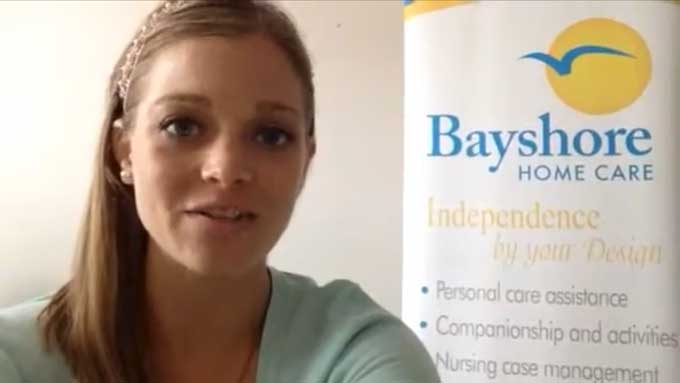 Breck, a senior care specialist, gives a tip while standing by a Bayshore Home Care banner