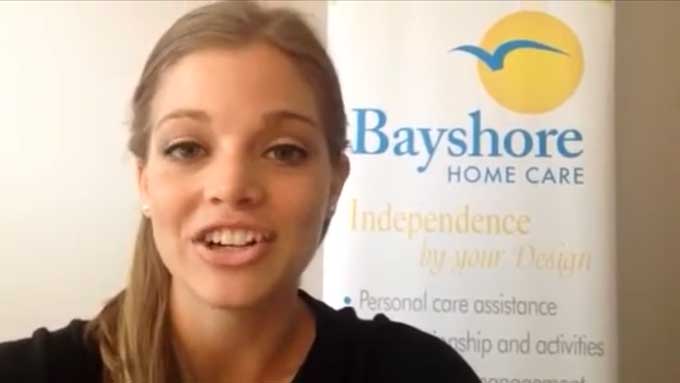 Breck, a senior care specialist, gives a tip while standing by a Bayshore Home Care banner