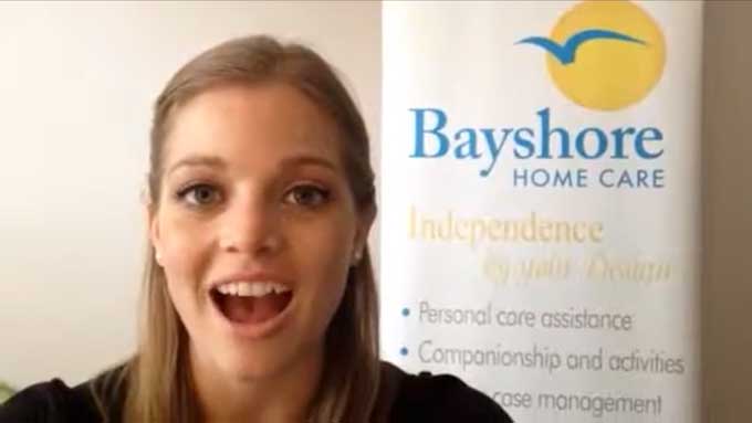 Breck, a senior care specialist, gives a tip while standing by a Bayshore Home Care banner