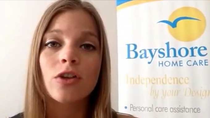 Breck, a senior care specialist, gives a tip while standing by a Bayshore Home Care banner