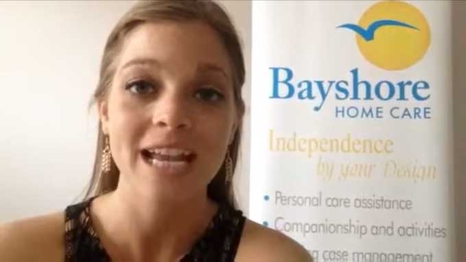 Breck, a senior care specialist, gives a tip while standing by a Bayshore Home Care banner