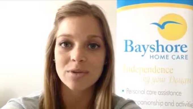 Breck, a senior care specialist, gives a tip while standing by a Bayshore Home Care banner